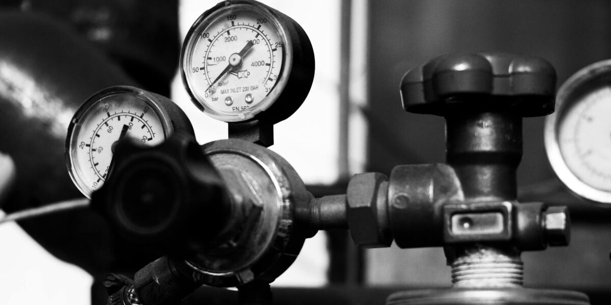 A close-up of a brass air pressure gauge showing kPa readings, symbolizing the debate over pressure as a temperature cause.