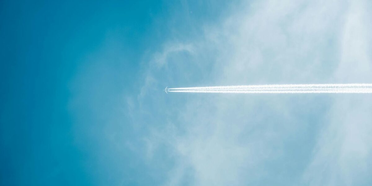 An airplane leaving contrails in a blue sky above an airport, symbolizing the deportation flights climate impact from ICE operations.