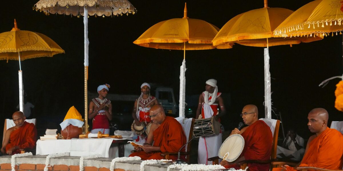Senior Sri Lankan Buddhist monk in orange robes walks past a sacred fig tree at a temple, sri lanka monk suspended case