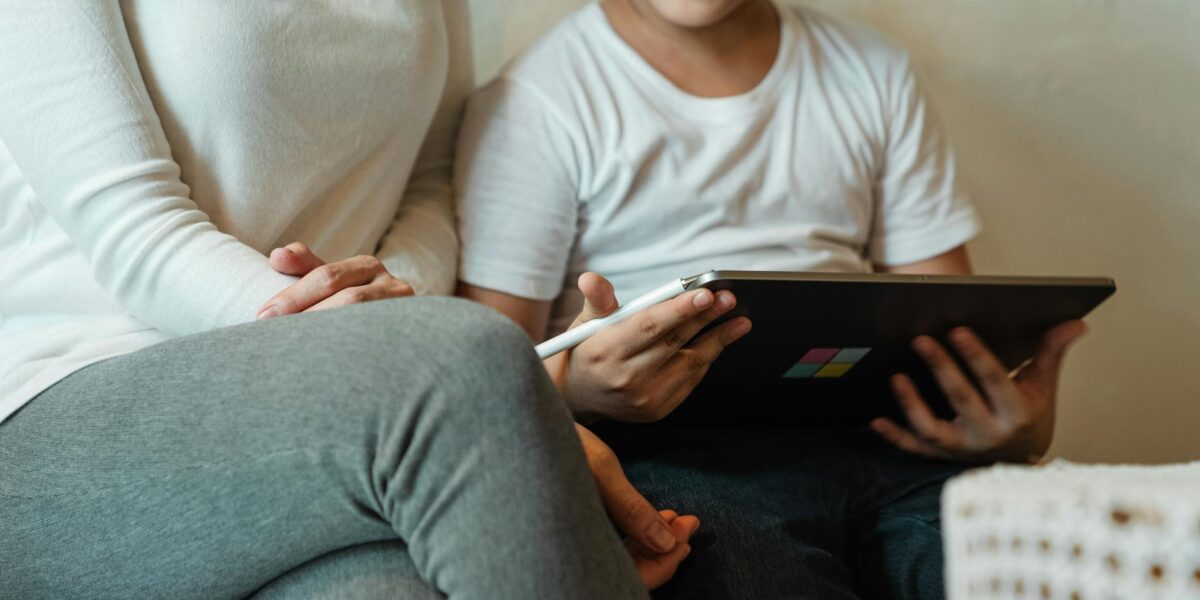 A young child using a tablet while a parent supervises, illustrating the need for child safety online in digital spaces.