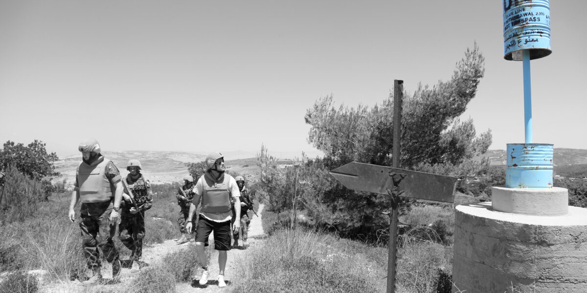 A UN peacekeeper patrols near a chain-link fence marking the Blue Line tensions between Lebanon and Israel.
